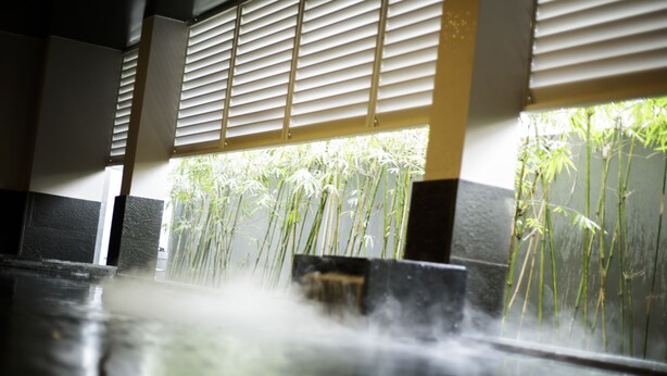 Un espace de détente avec un élément aquatique, des plantes en bambou et une vue sur l’extérieur à travers une fenêtre munie de stores.