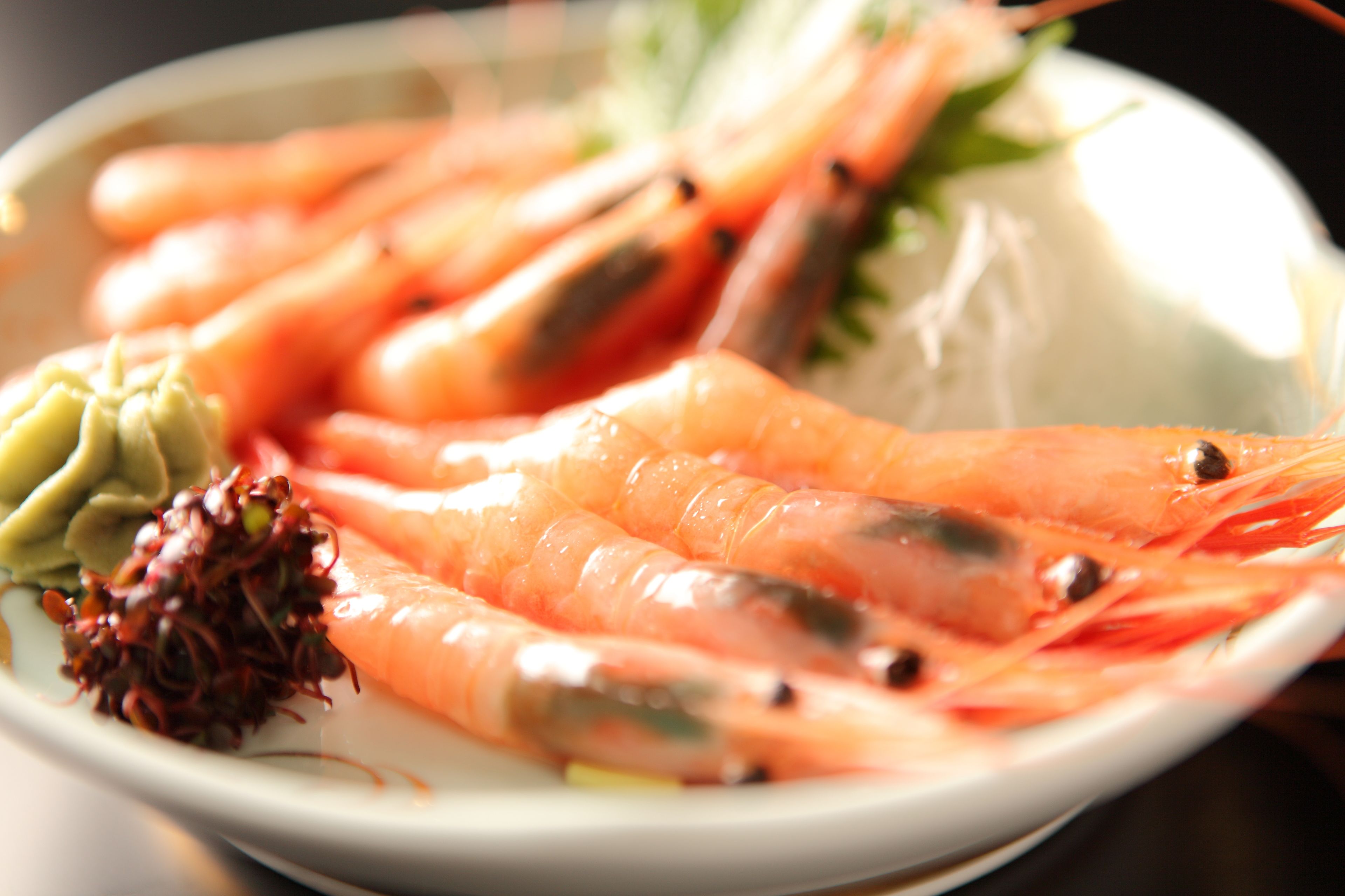 Un plato de camarones cocidos, adornado con hierbas verdes y un pequeño vegetal rojo.