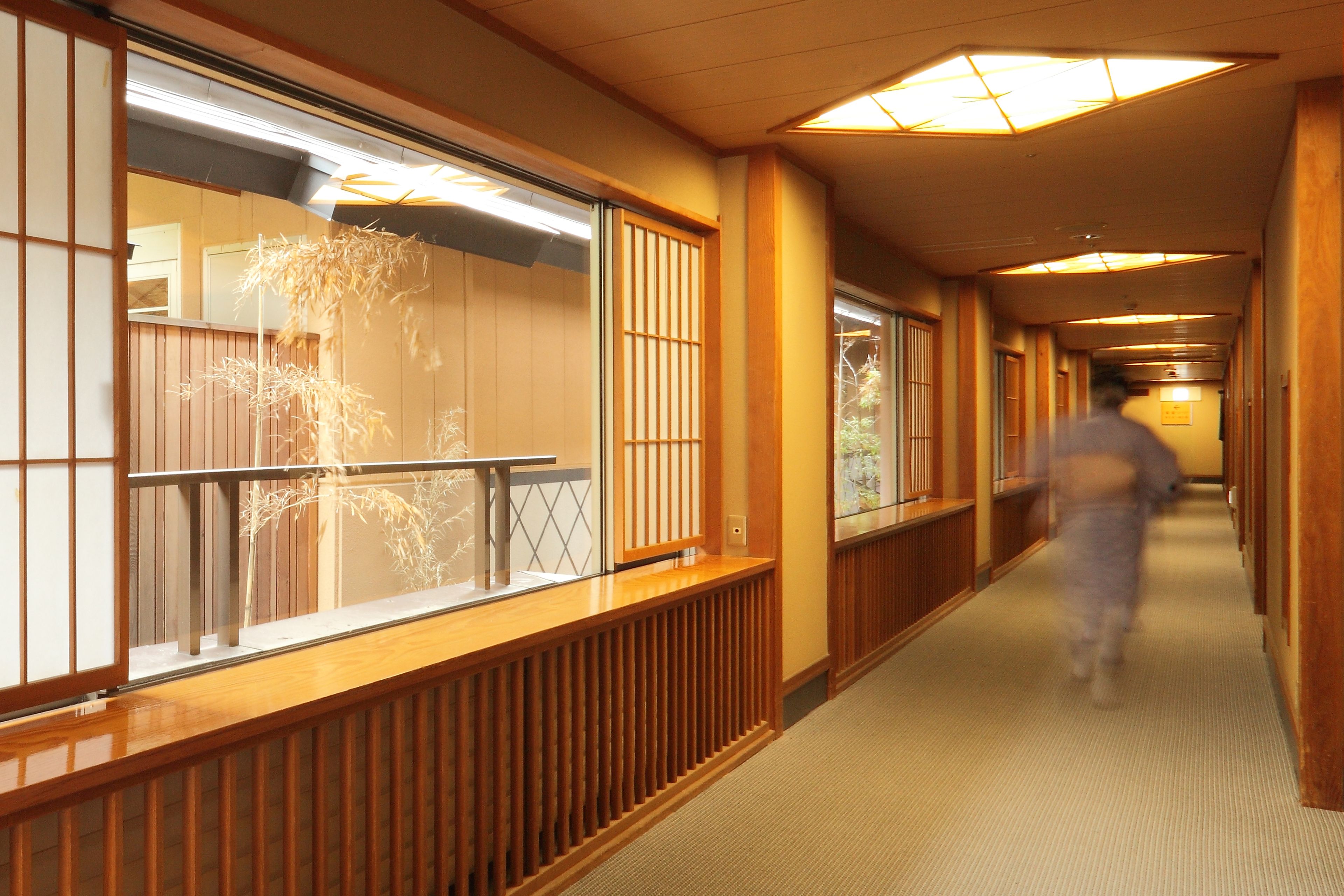 A corridor with wooden paneling, a glass railing, and a person walking.
