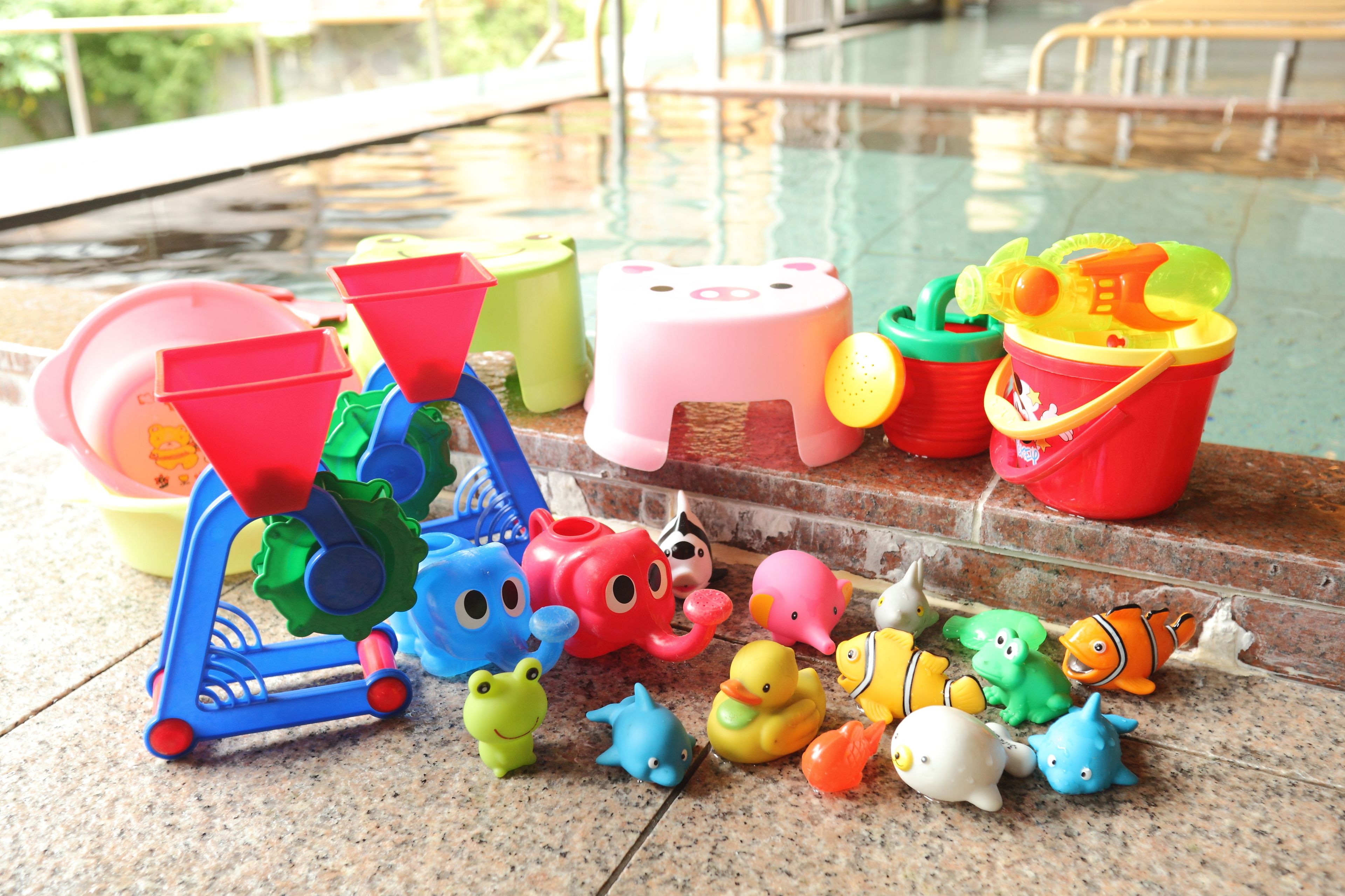 Variedad de juguetes y equipo de juegos infantiles de colores cerca de una piscina.
