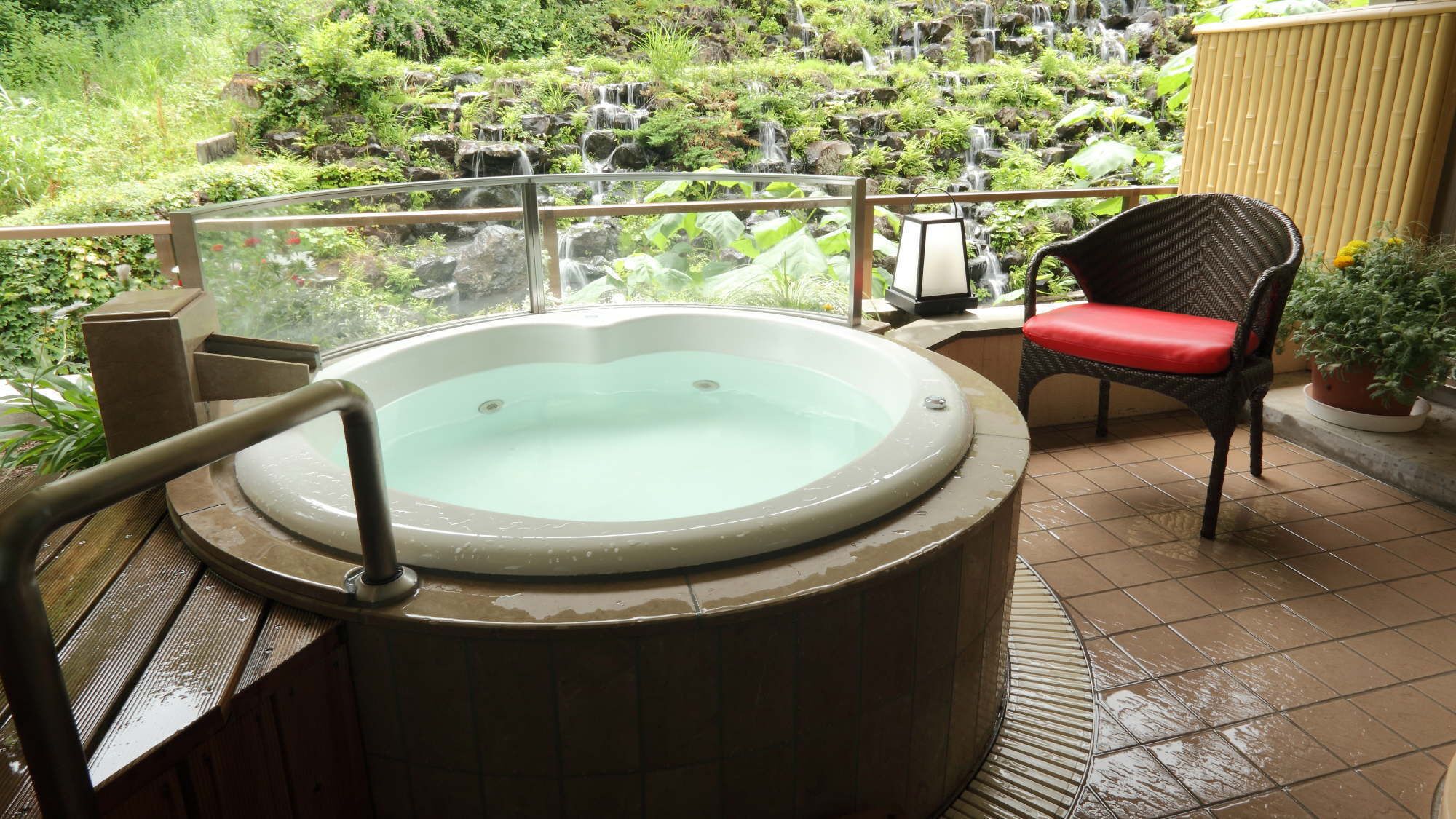 Een bubbelbad op een balkon met uitzicht op een waterval en groen.