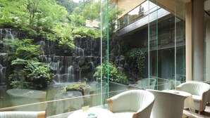 A glass-enclosed area with a waterfall, seating, and a view of a building.