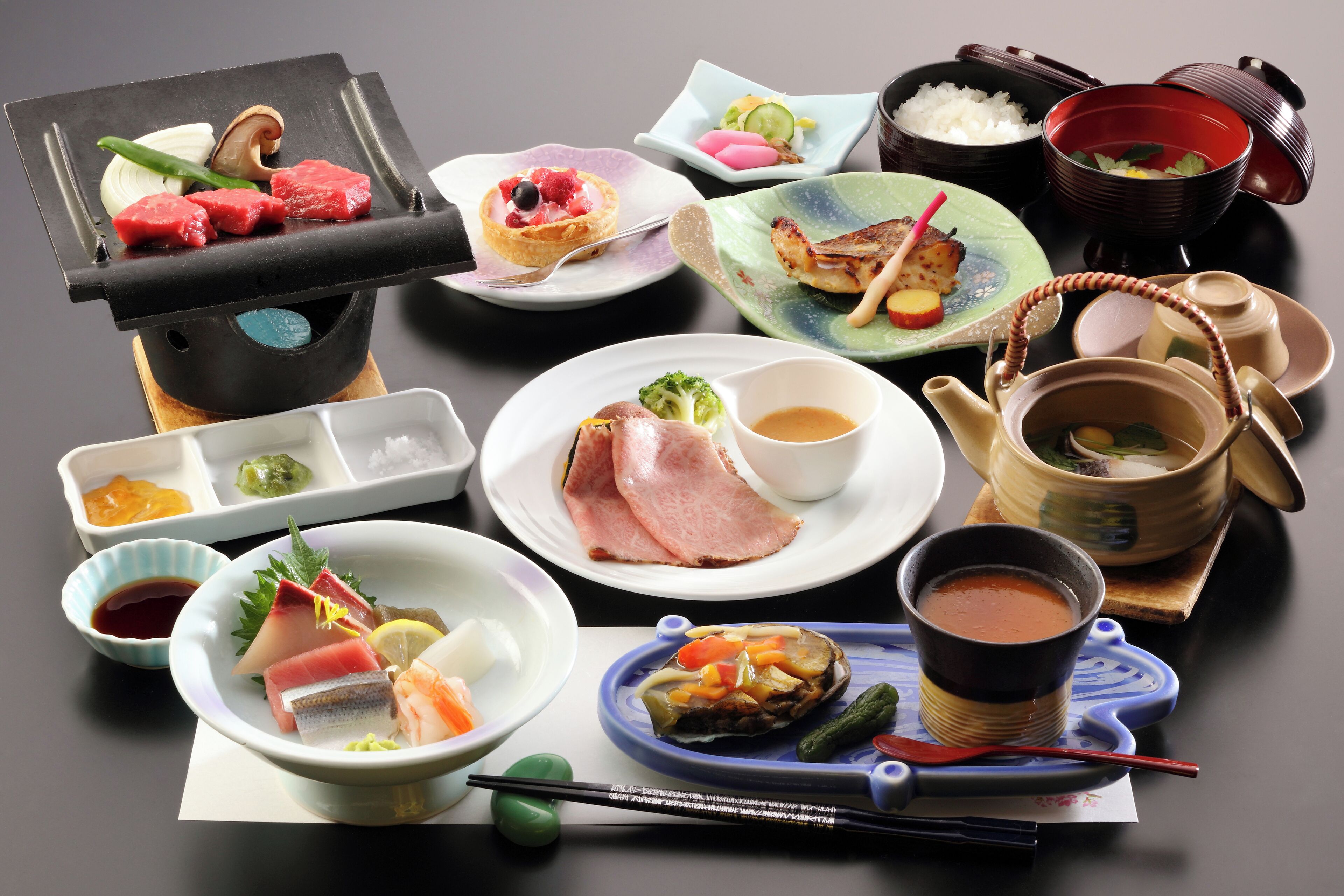Diversos plats japonesos, com sushi, sashimi i una olla japonesa, disposats sobre una taula.