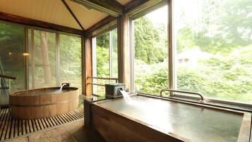 A wooden bathtub with a faucet, large windows, and a view of a forested area.