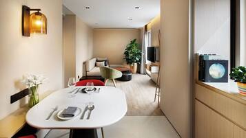 A modern hotel room with a dining area, a sofa, a TV, and a window with a view.