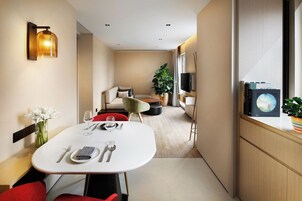 A modern hotel room with a dining area, a sofa, a TV, and a window with a view.