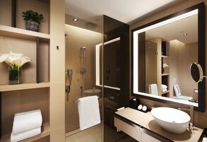 A modern bathroom with a large mirror, a white sink, and a glass-enclosed shower.
