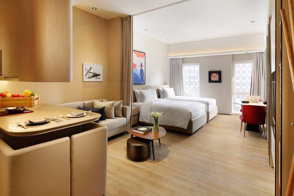 A modern hotel room with a sofa, a dining area, a bed, and a desk.
