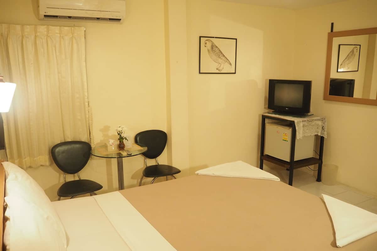 A hotel room with a bed, a desk with two chairs, a television on a stand, and a wall-mounted air conditioner.