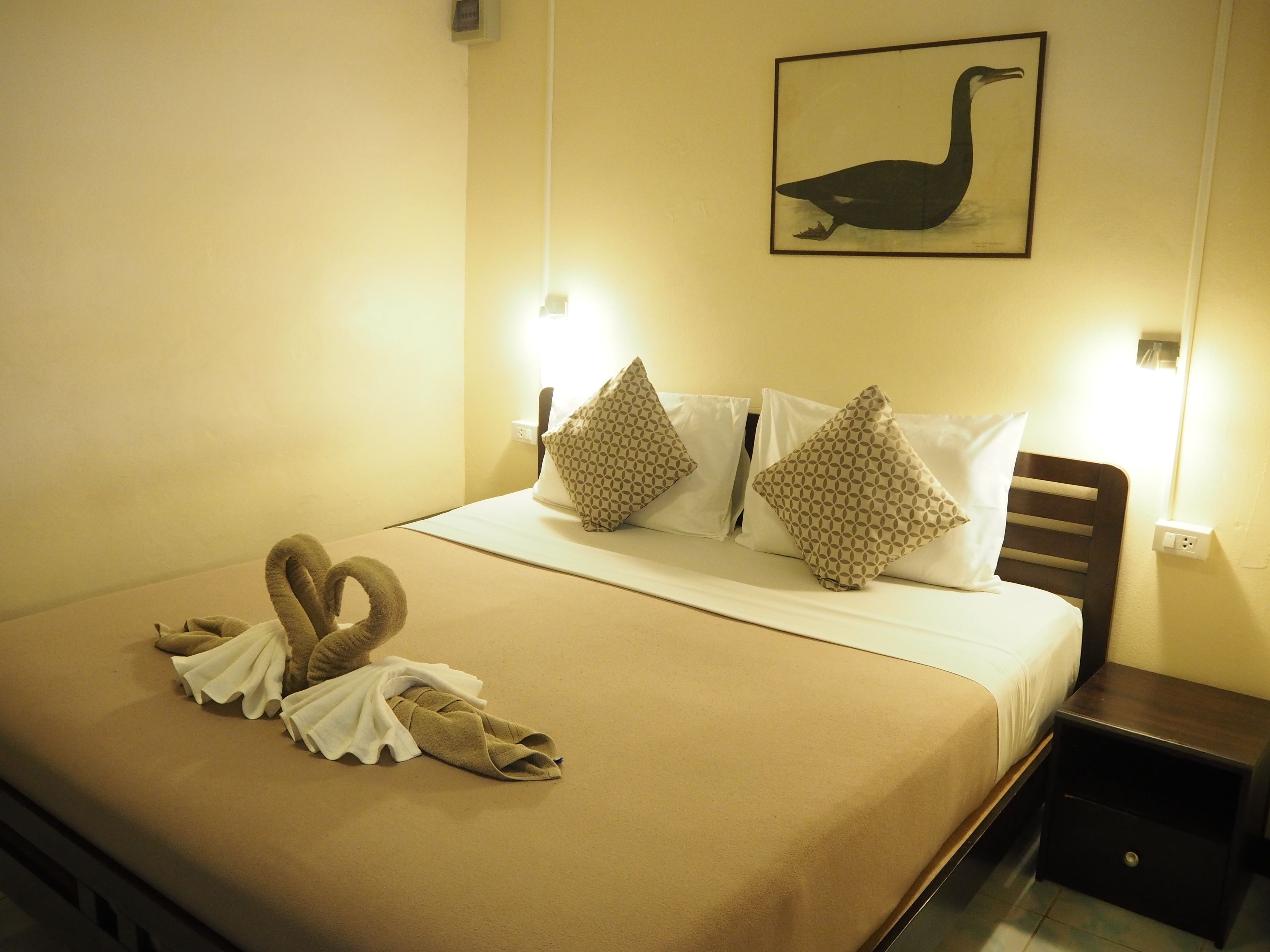 Habitación de hotel con cama, almohadas, un arreglo de toallas y un cuadro de un pájaro colgado en la pared.