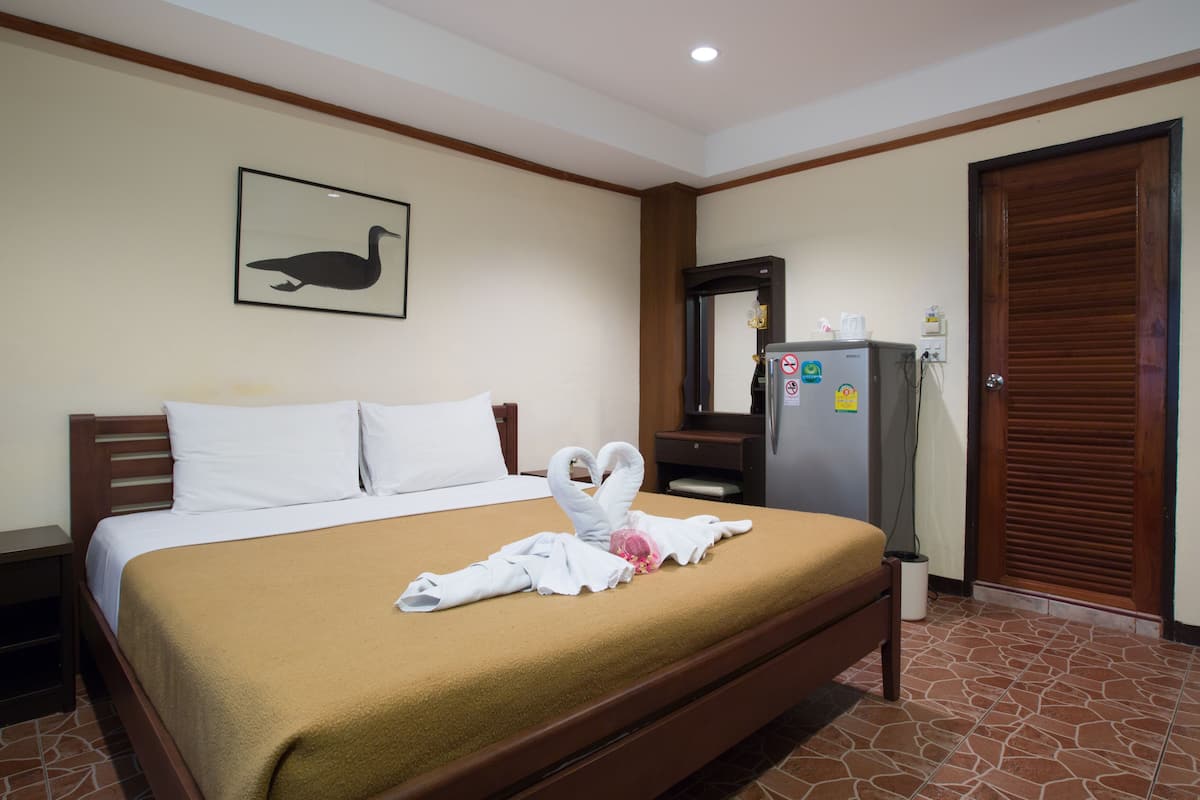 A hotel room with a bed, a refrigerator, a wooden door, and a framed picture on the wall.