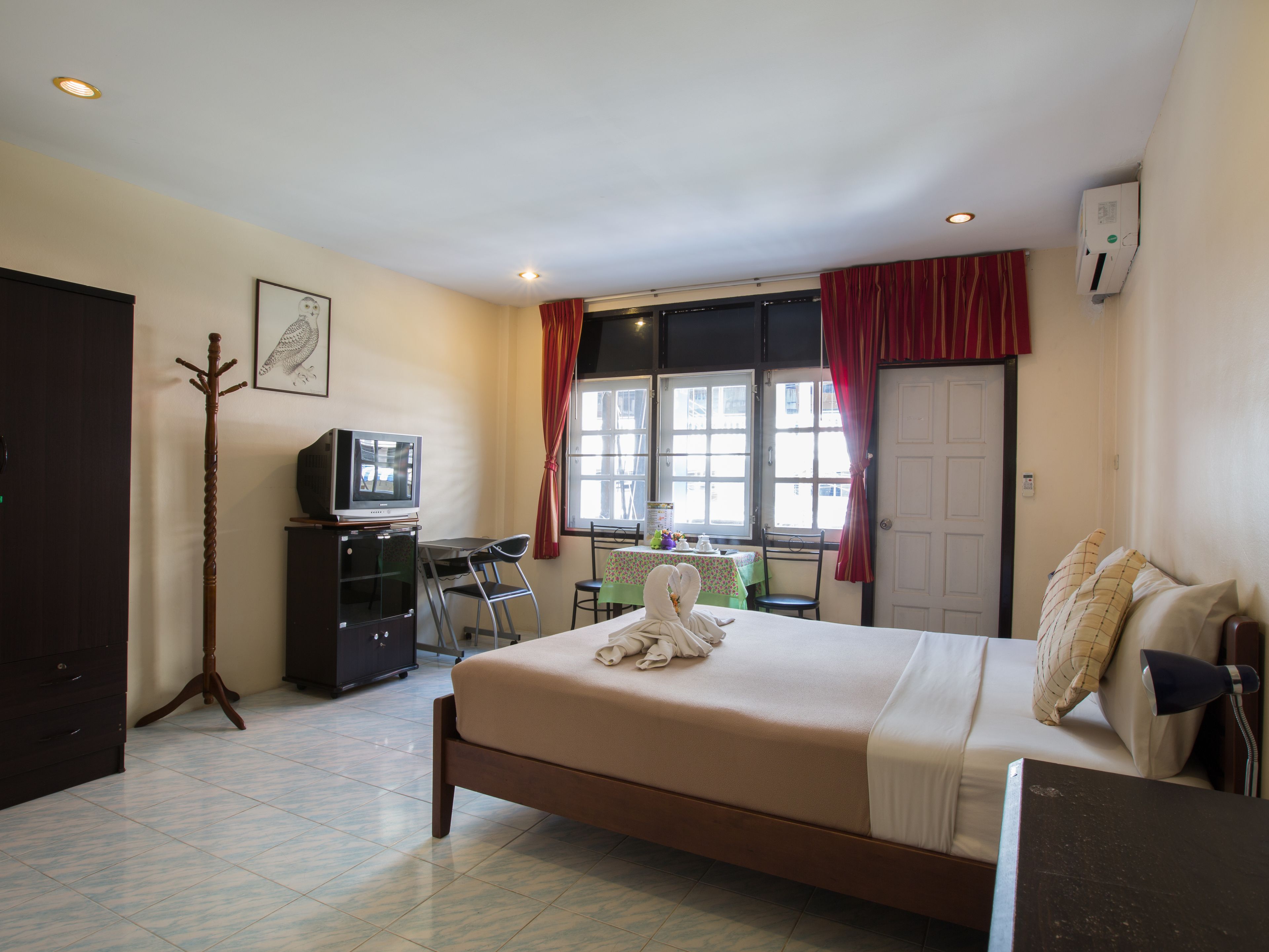 A hotel room with a bed, a desk, a chair, a television, and a coat rack.
