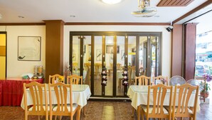 A restaurant interior with wooden chairs and tables, a tiled floor, and a view through a glass door. - Stefans Guesthouse (Pattaya)