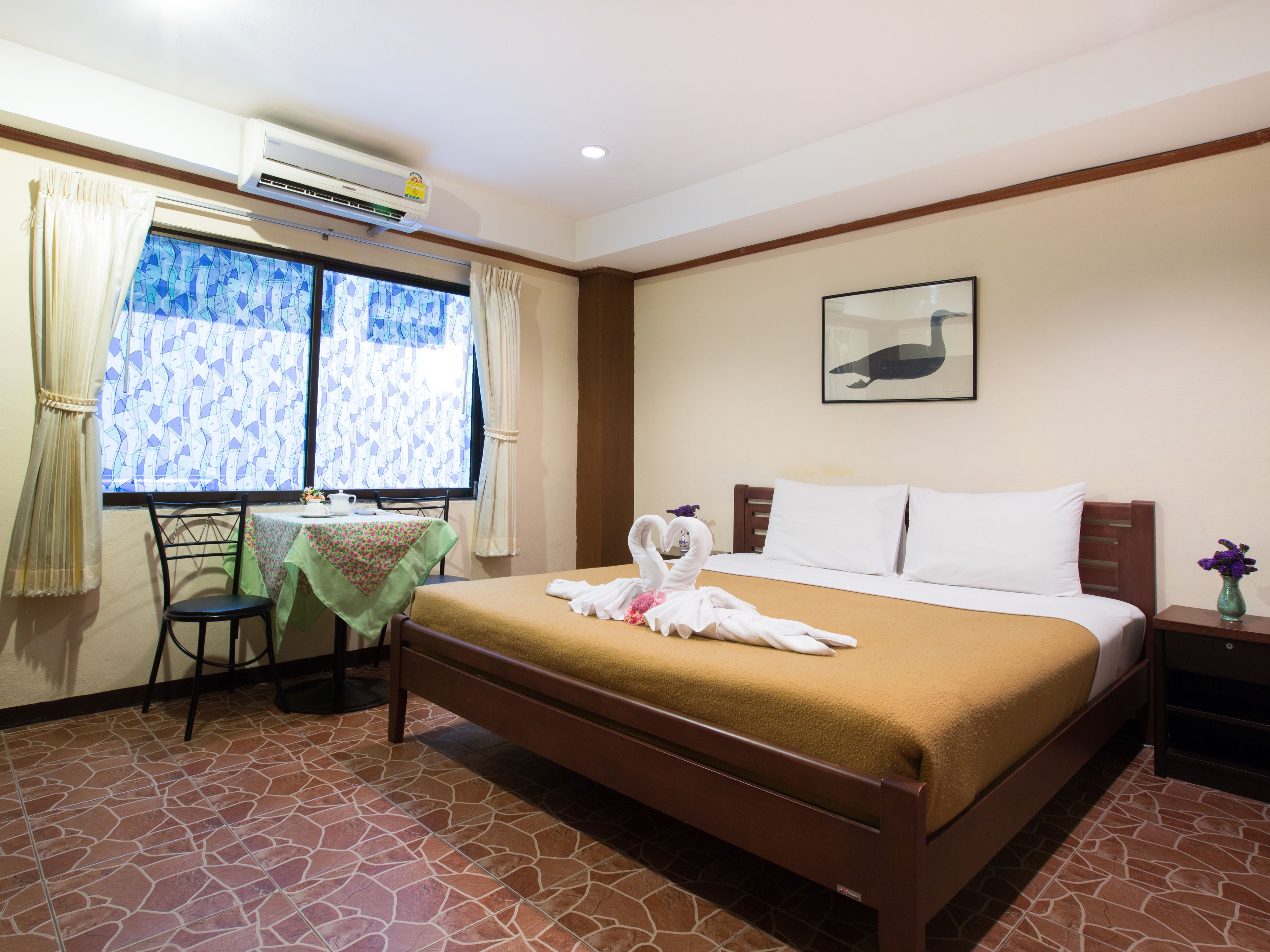 A hotel room with a bed, a desk with a chair, a window with curtains, and a wall-mounted picture.