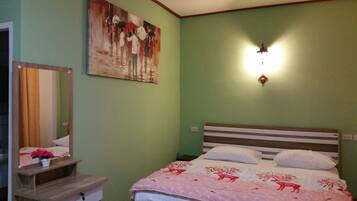 Um quarto com cama, mesa de cabeceira, espelho, luminária na parede e um quadro.