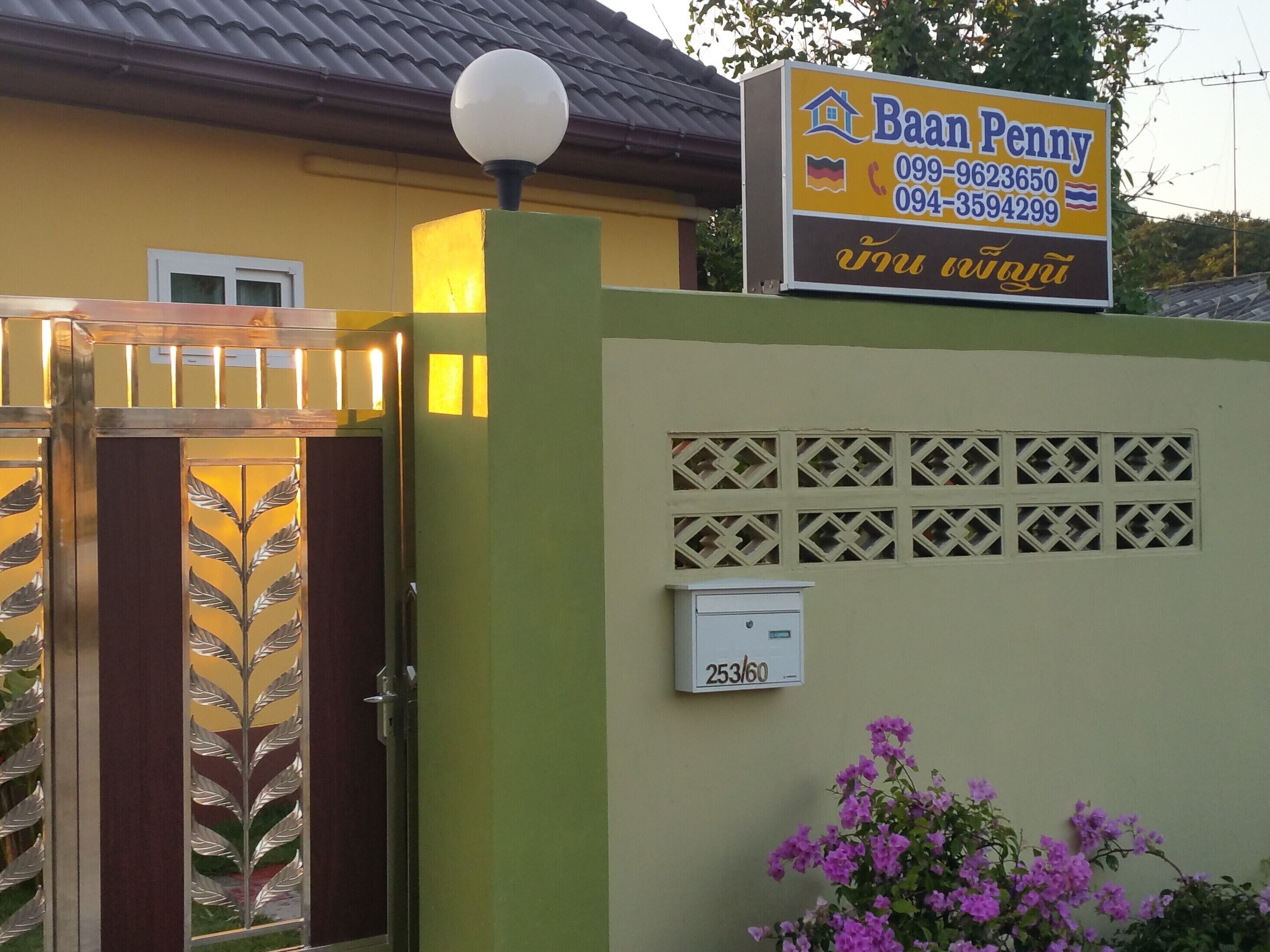 Una entrada cerrada con un letrero que dice Baan Penny, una caja de servicios públicos y una jardinera.