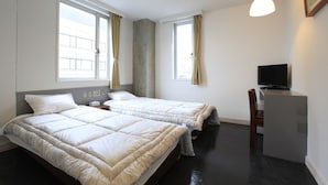 Een hotelkamer met twee bedden, een bureau met een televisie en grote ramen met gordijnen.