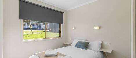 A bedroom with a bed, a window with a view of a house, a bedside table, and a nightstand.