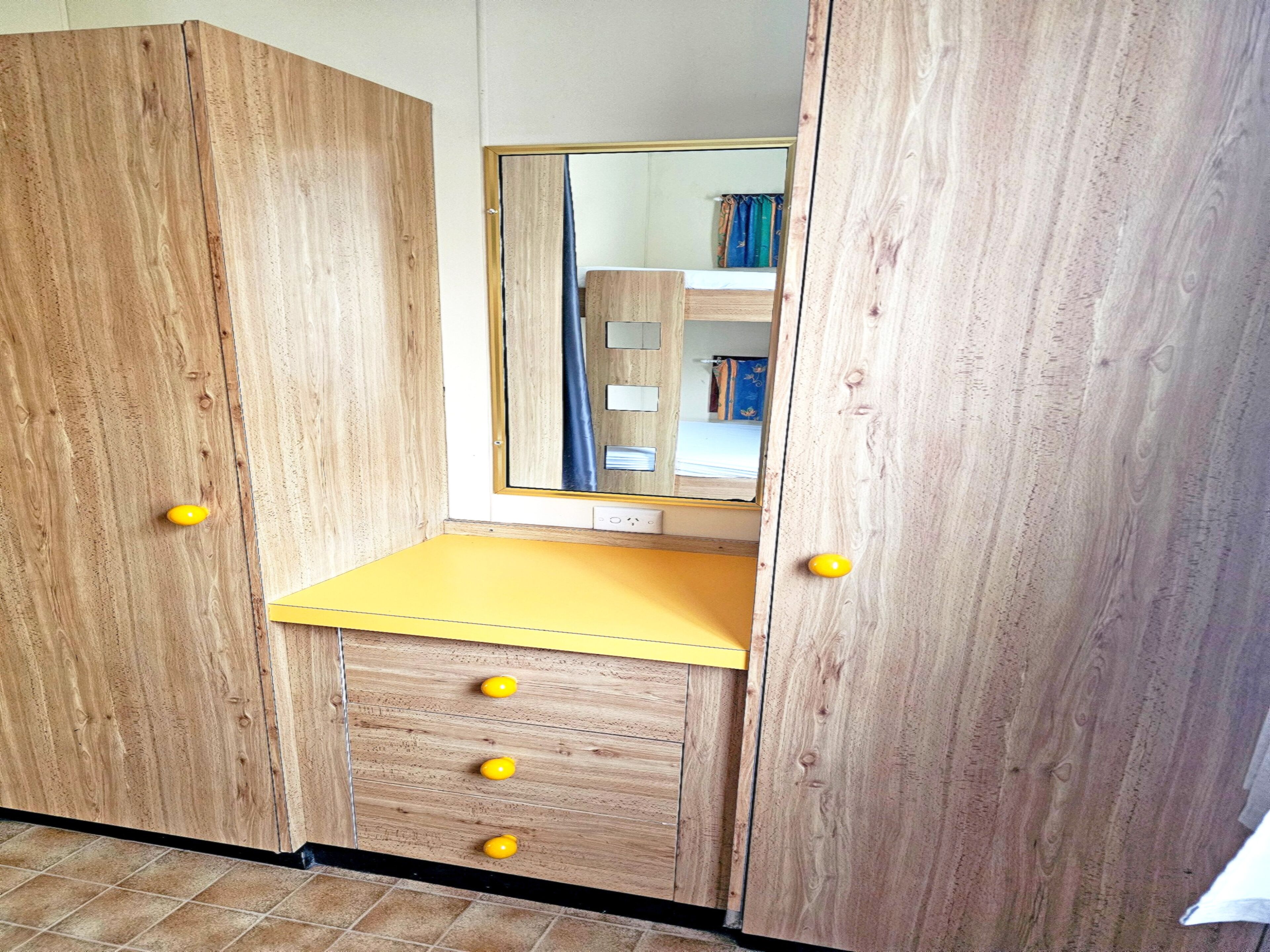 A wooden wardrobe with a mirror, a yellow countertop, and four drawers.