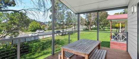 A wooden deck with a table and bench, overlooking a grassy area and a road with cars.