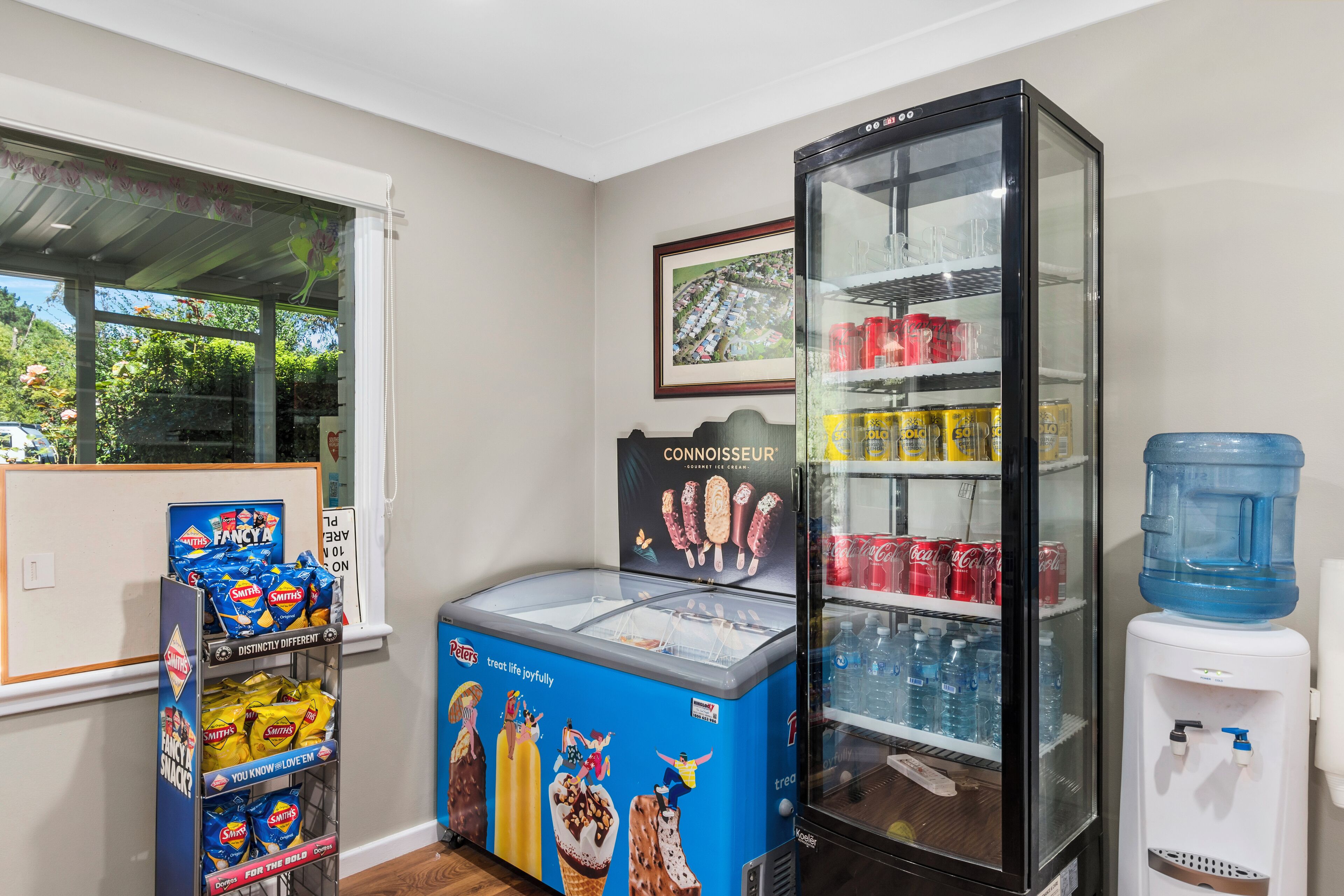A room with a refrigerator stocked with beverages, a water dispenser, and a snack display.