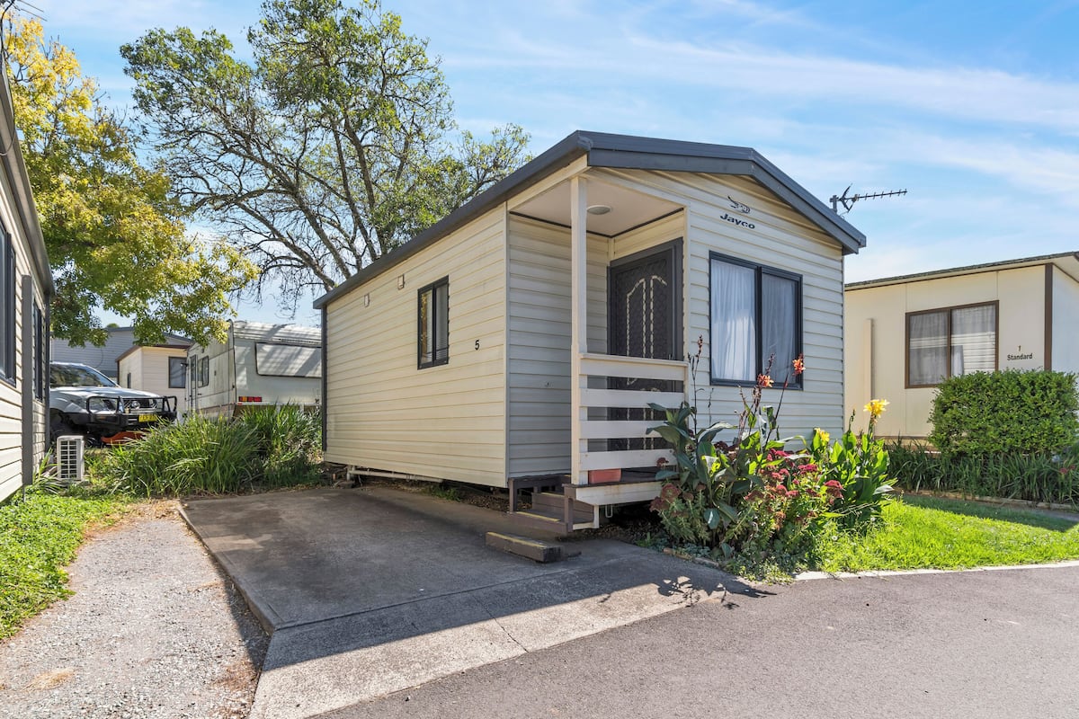A mobile home with a porch, a small deck, and a garden with flowers and shrubs.