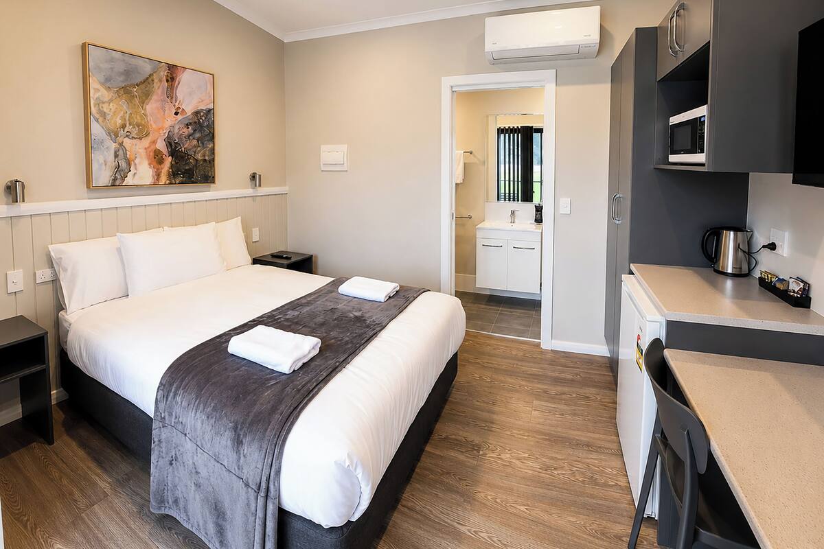 A hotel room with a bed, bedside tables, a desk, a microwave, and a coffee maker.