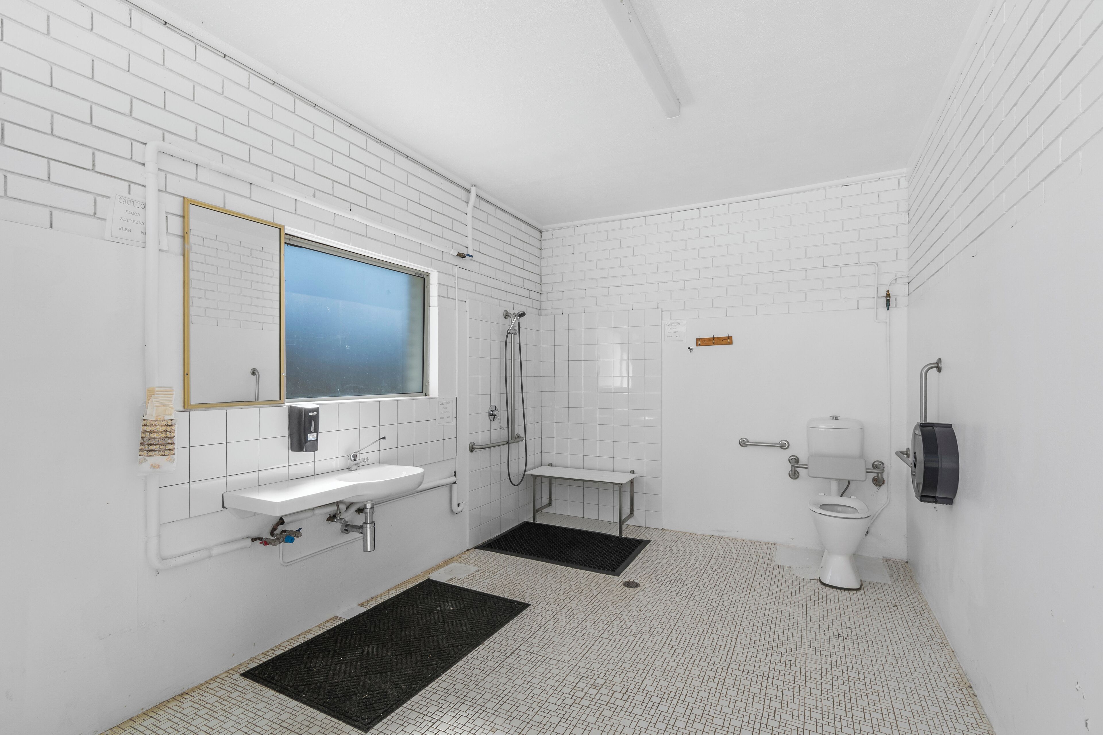 A modern bathroom with white tiled walls, a sink, a mirror, a toilet, and a shower.