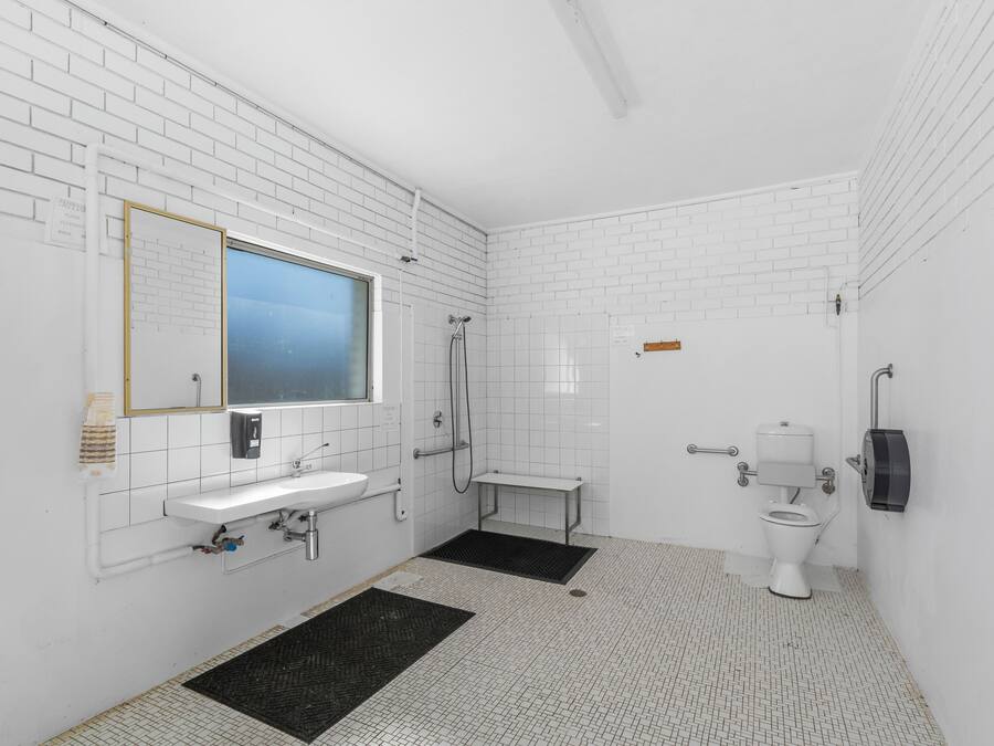 A modern bathroom with white tiled walls, a sink, a mirror, a toilet, and a shower.