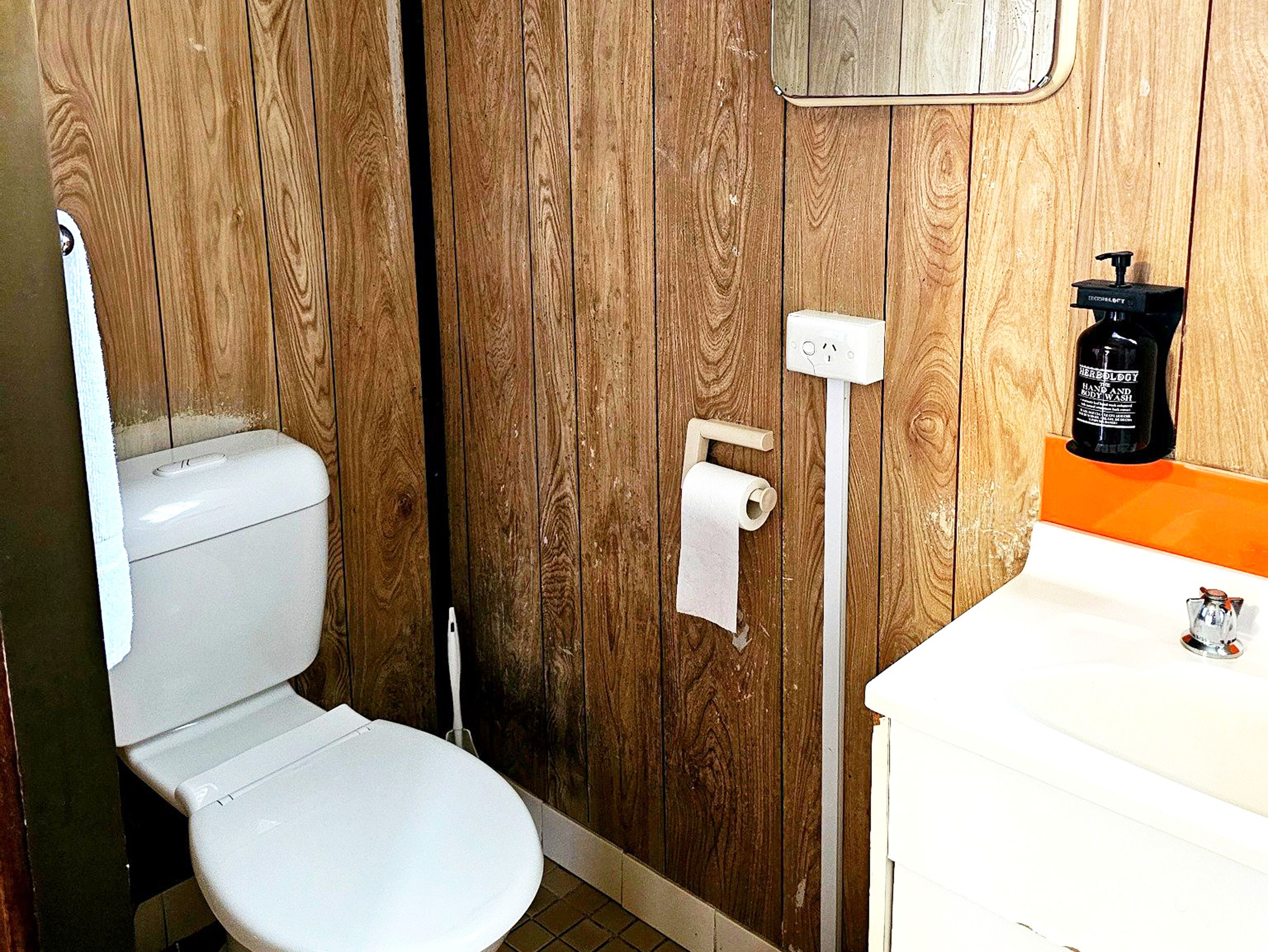 A wooden-paneled bathroom with a toilet, a hand soap dispenser, and a paper towel dispenser.