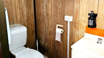A wooden-paneled bathroom with a toilet, a hand soap dispenser, and a paper towel dispenser.