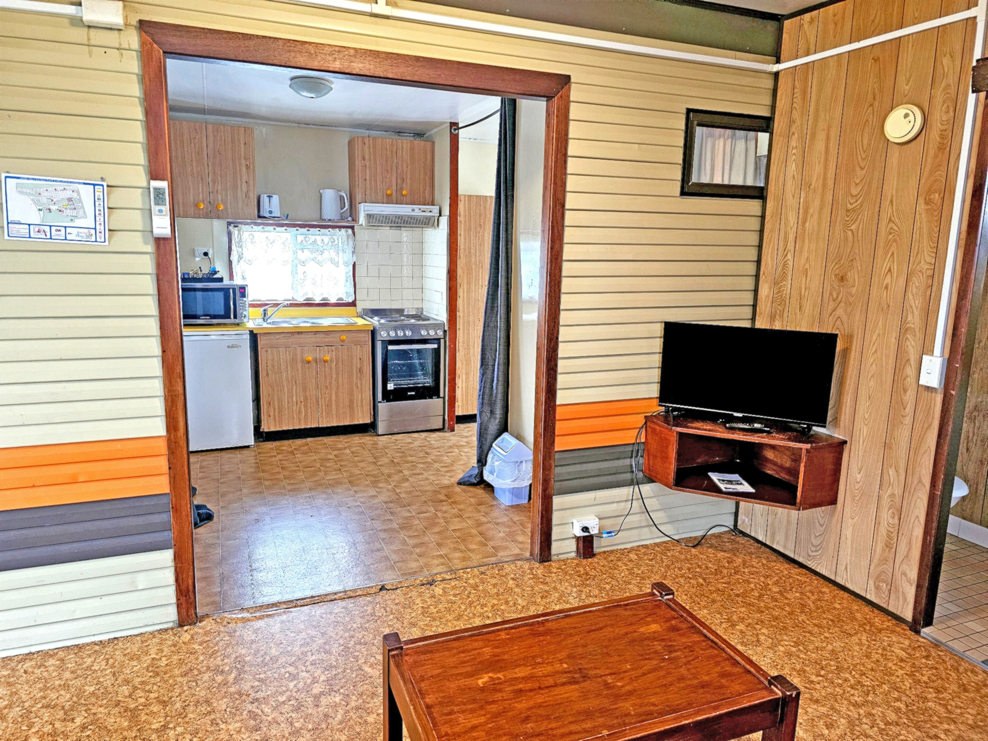 Een compacte leefruimte met een kitchenette, een televisie en een houten tafel.