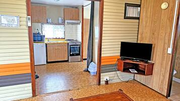 Een compacte leefruimte met een kitchenette, een televisie en een houten tafel.