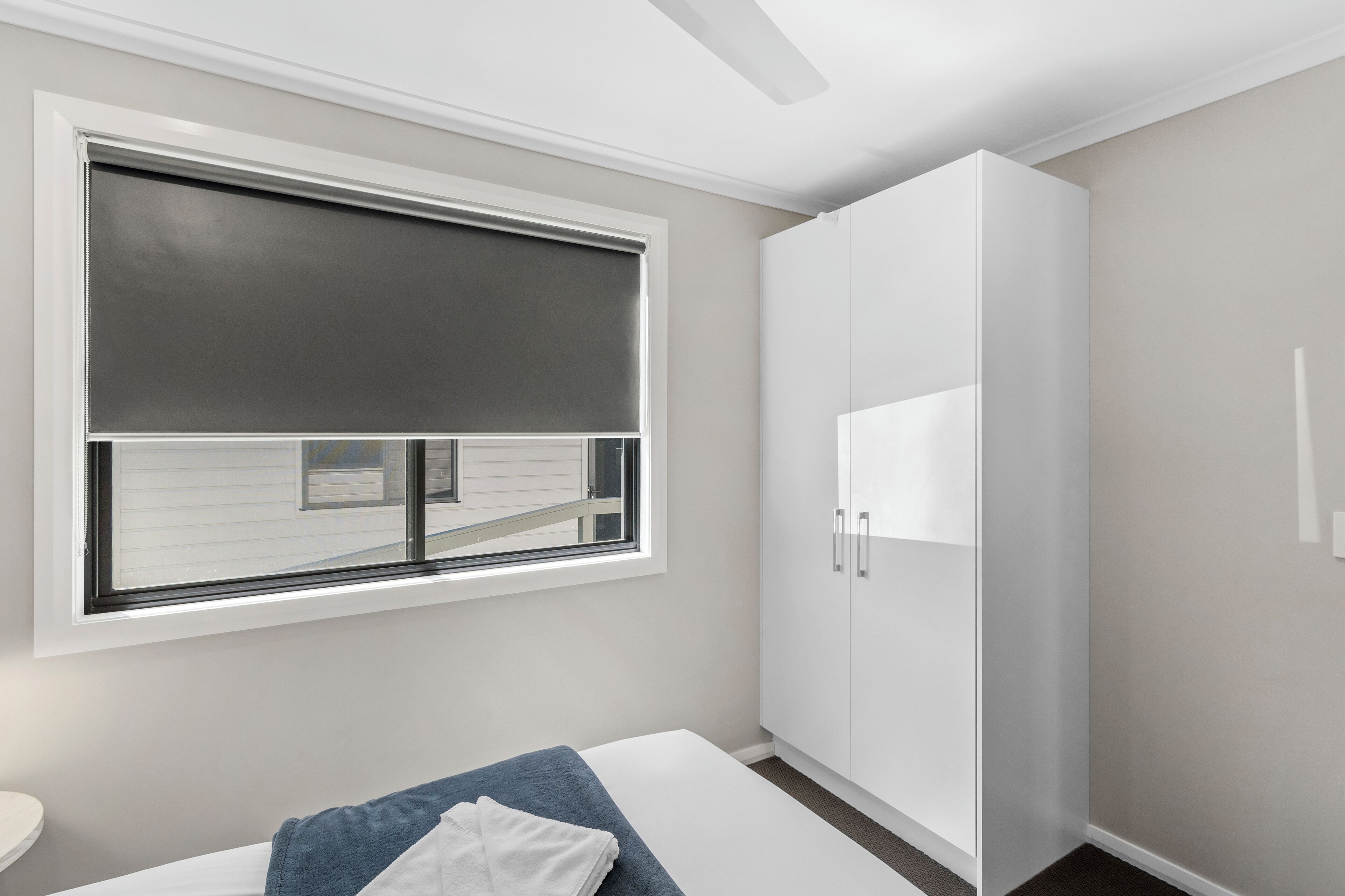 A bedroom with a bed, a window with blinds, a wardrobe, and a ceiling fan.