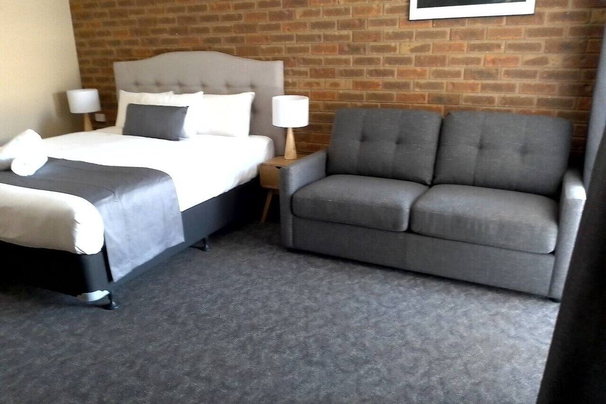 Habitación de hotel con cama, sofá gris, pared de ladrillo y un cuadro en la pared.