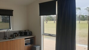 A modern kitchen with a sink, microwave, and toaster. There is a window with a view of a grassy area. - Lara Lodge (Lara)