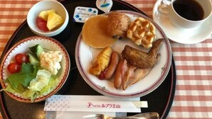 Un plateau contenant divers éléments pour le petit-déjeuner, notamment des crêpes, des saucisses, des gaufres, une salade et une tasse de café.