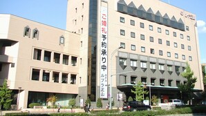 Un hôtel à plusieurs étages, doté d’une enseigne verticale bien visible en japonais, d’une architecture moderne avec un toit plat et d’un espace de stationnement à l’avant.