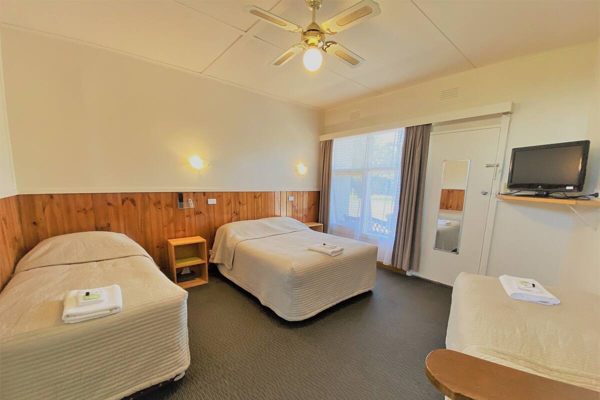 A hotel room with two beds, a television, and a window with curtains.