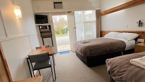 Una habitación de hotel con cama, escritorio, silla, microondas y ventana con cortinas.