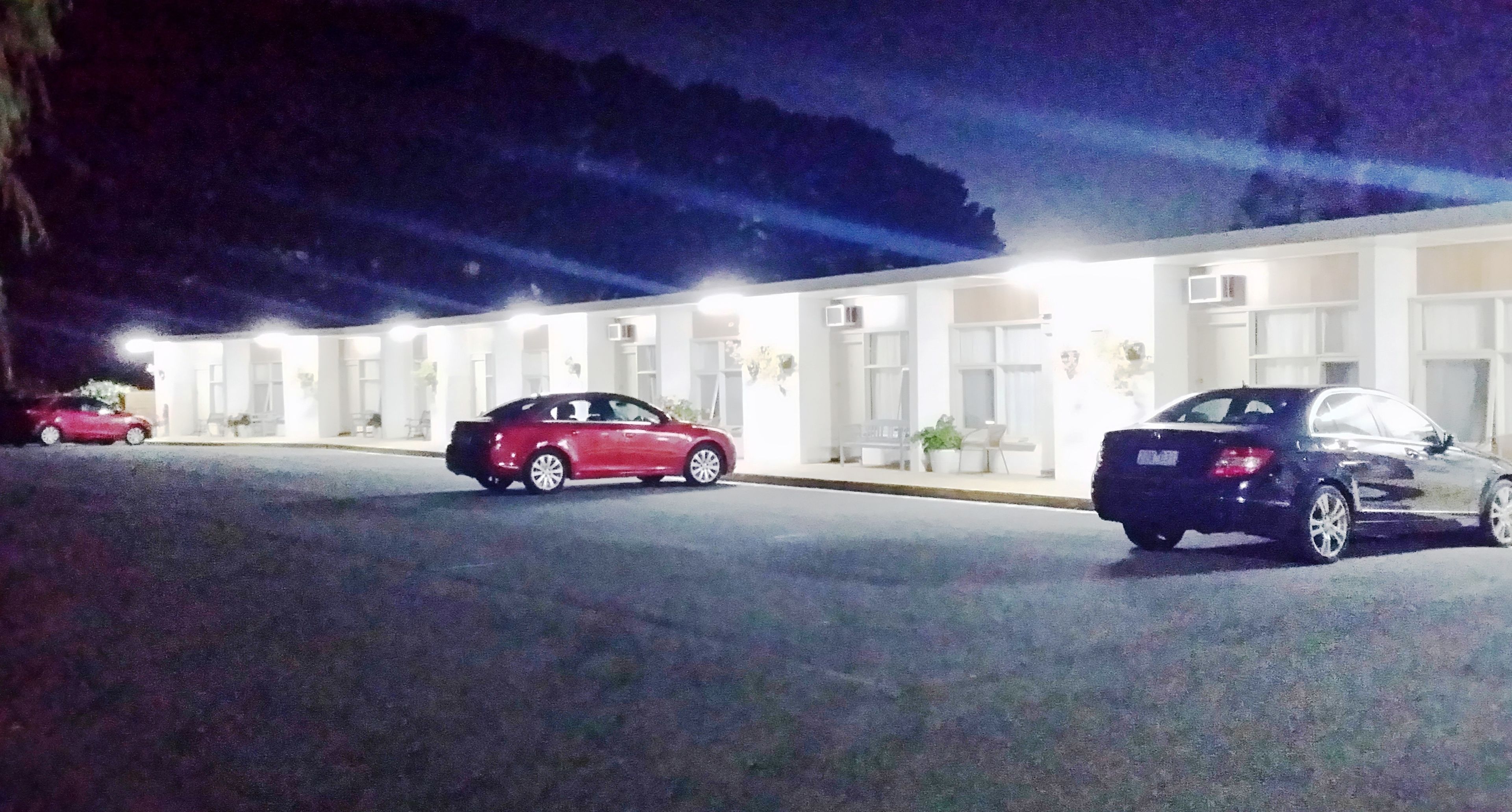 A hotel with a row of rooms, a parking lot, and a building with a flat roof.