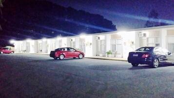 A hotel with a row of rooms, a parking lot, and a building with a flat roof.