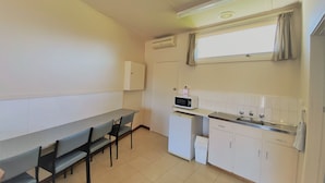Una pequeña kitchenette con microondas, pileta y alacenas. Hay una mesa de comedor con sillas y una ventana con cortinas.