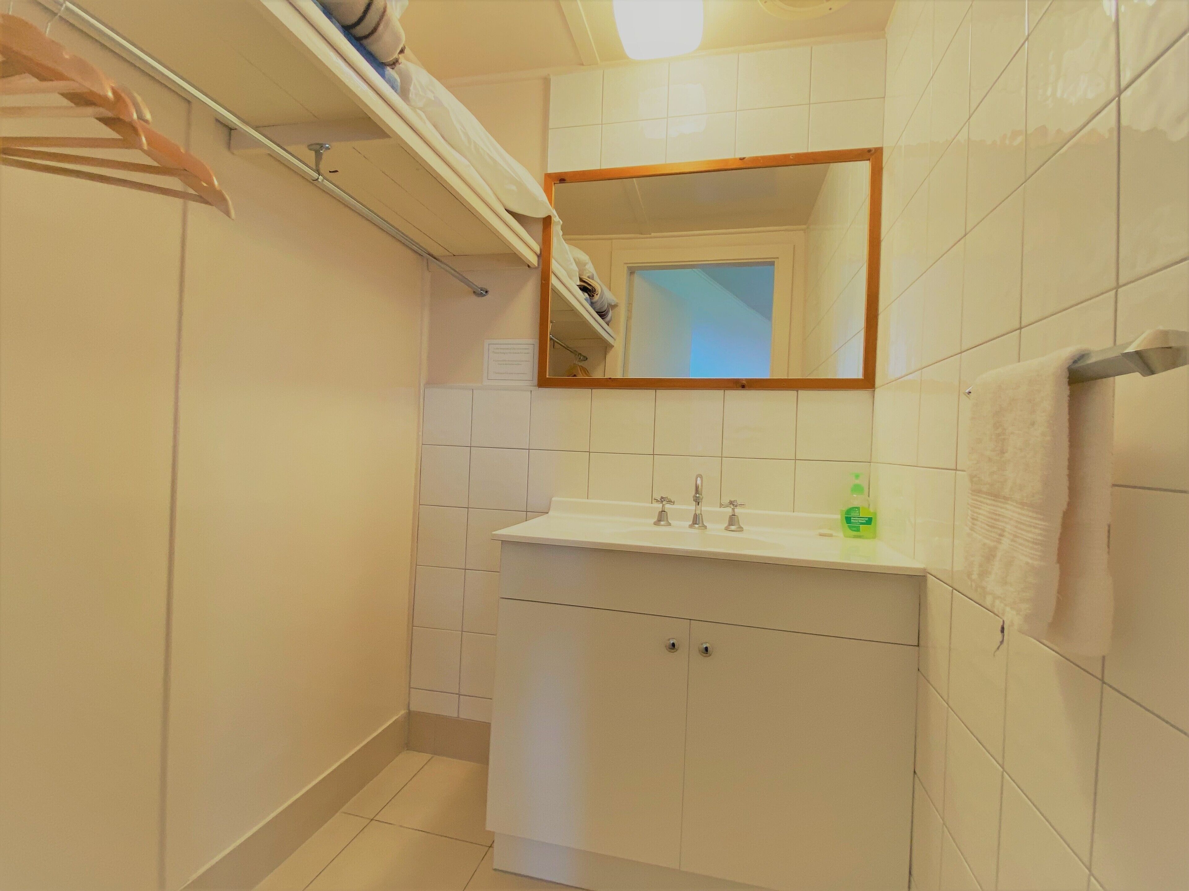 Uma casa de banho com uma pia branca, duas torneiras, um espelho e um porta-toalhas.