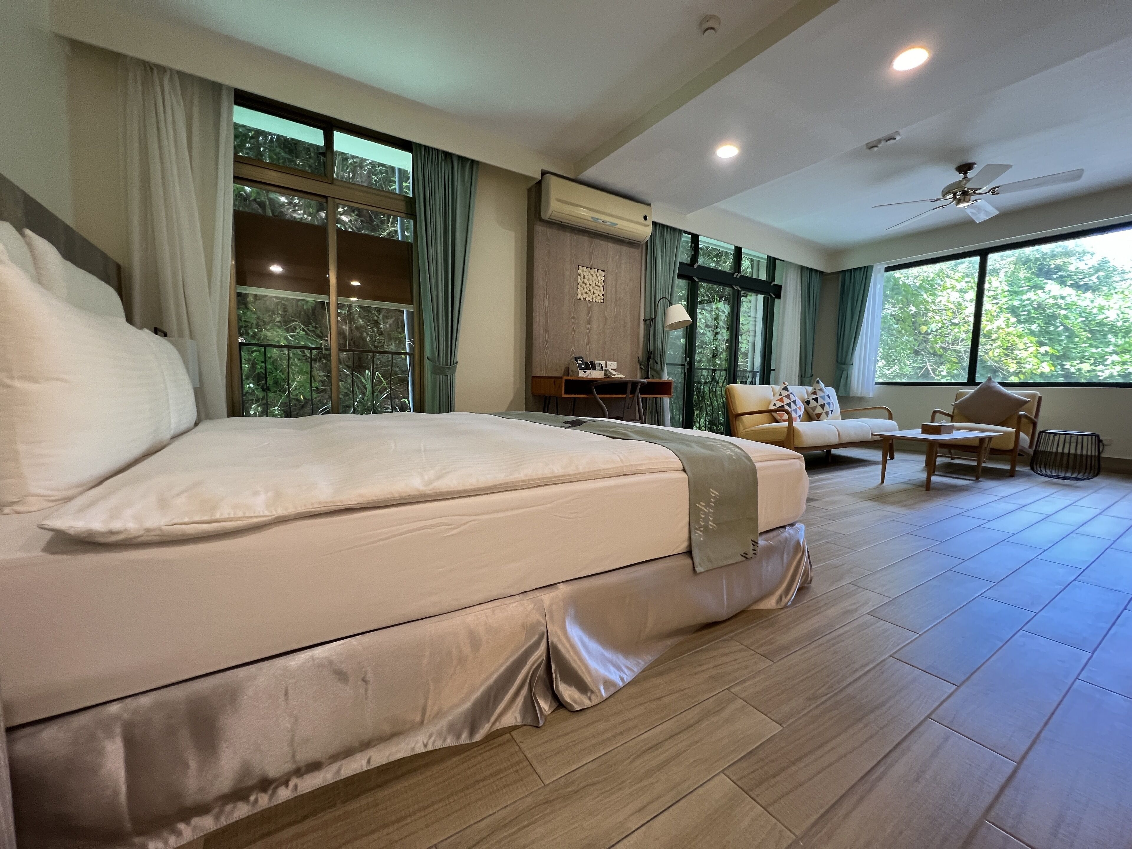 A spacious bedroom with a large bed, a desk, and a comfortable seating area by a large window.