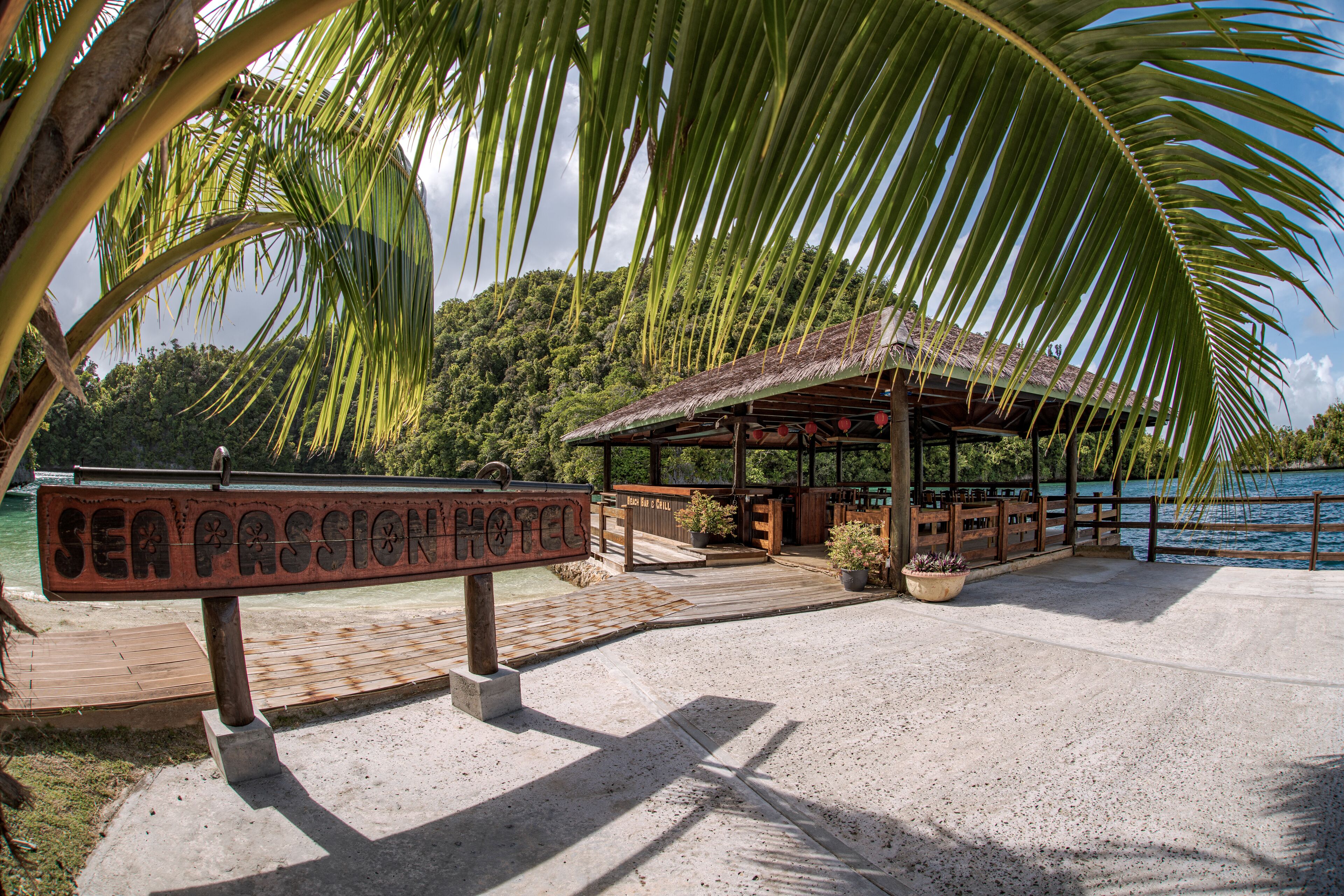 A wooden signboard for Sea Passion Hotel, a wooden structure with a thatched roof, and a beach area with palm trees.
