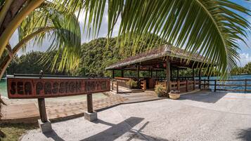 A wooden signboard for Sea Passion Hotel, a wooden structure with a thatched roof, and a beach area with palm trees.