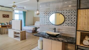 A modern hotel room with a wooden floor, a bed with a white headboard, a round mirror, a black marble sink, and a wooden cabinet.