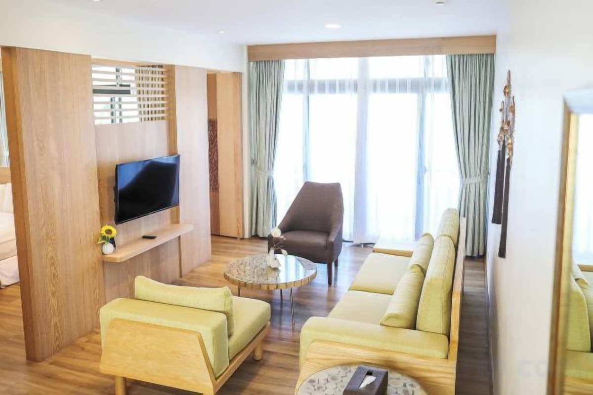 Habitación de hotel con sofá, sillón, televisión y un ventanal con cortinas.
