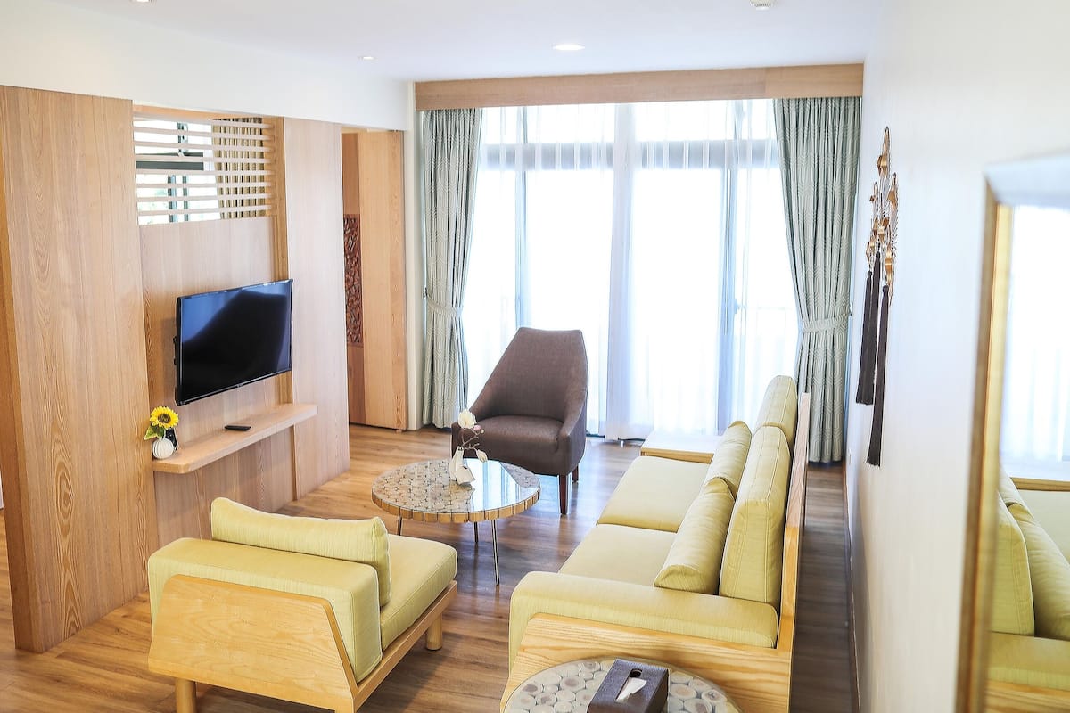 Een hotelkamer met een houten vloer, een zithoek, een televisie op een houten standaard, een bijzettafeltje en een bed met hoofdbord.